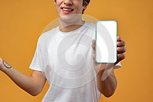 Smiling young man showing mobile phone blank white screen mockup to camera.