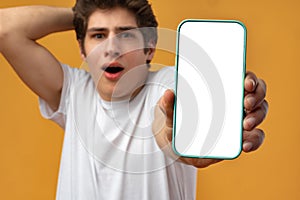 Smiling young man showing mobile phone blank white screen mockup to camera.