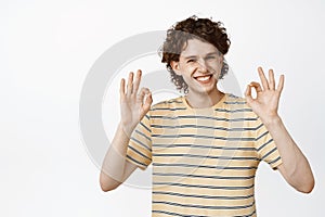 Smiling young man showing okay, zero gesture, say no problem, approve something, standing over white background