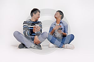 Smiling young man showing smart phone to ecstatic girlfriend while sitting against white background