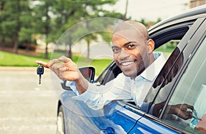 Smiling, young man sitting in his new car showing keys