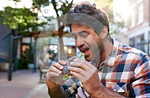 Smiling young man sitting outside eating a delicious bagel photo