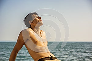 Smiling young man sitting by sea or ocean shore