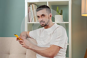 smiling young man sitting on a sofa looking at social media with a smartphone