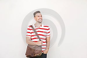 Smiling young man standing against white wall with bag