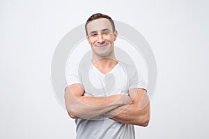 Smiling young man standing with arms crossed against gray background