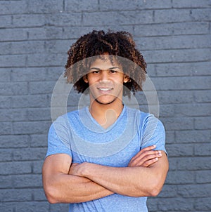 Smiling young man standing with arms crossed against gray wall