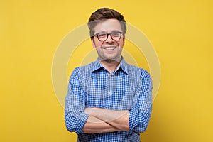 Smiling young man standing with arms crossed against yellow background.