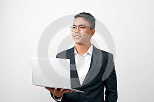 Smiling young man standing in black suit and glasses, holding open laptop