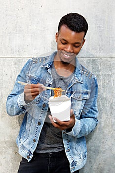 Smiling young man standing with box of noodles and chopsticks