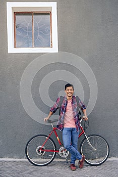 Smiling young man standing with his bike against a wall