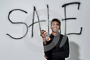 Smiling young man standing near graffiti on white wall