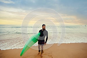 Smiling young man with surfboard on the beach. Boy coming out of the ocean after water surfing.