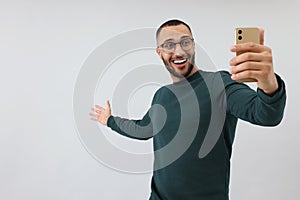 Smiling young man taking selfie with smartphone on grey background, space for text