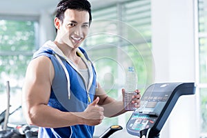 Smiling young man on treadmill holding water bottle