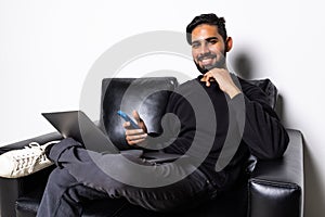 Smiling young man typing on mobile phone while sitting on a sofa at home with laptop