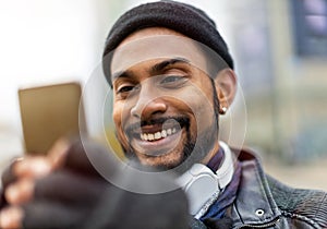 Smiling young man using smart phone outdoors at urban setting