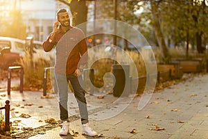 Smiling young man using smart phone outdoors at urban setting