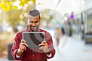 Smiling young man using tablet outdoors at urban setting