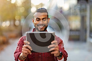 Smiling young man using tablet outdoors at urban setting