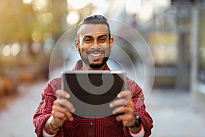 Smiling young man using tablet outdoors at urban setting