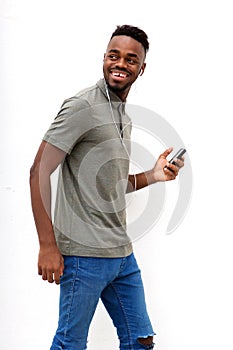Smiling young man walking with mobile phone and earphones against white background