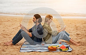 Smiling Young Man And Woman Messaging On Smartphones While Having Picnic Outdoors