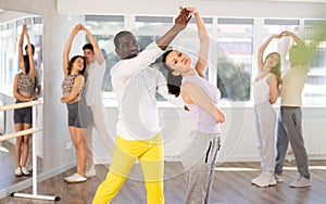 Smiling young man and woman with multinational group active people training energetic active swing dance movements in