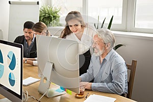 Smiling young manager helping senior worker with computer office