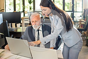 Smiling young manager helping senior worker with computer work in office