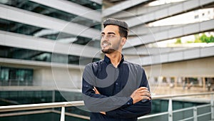 Smiling young Middle Eastern businessman stands confidently crossing arms outdoor