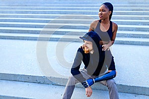smiling young mixed race couple in sportswear warming up outdoors sity background early morning