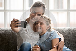 Smiling young mom cuddling little school adorable daughter, making selfie.