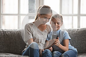 Smiling young mom and daughter using cellphone at home