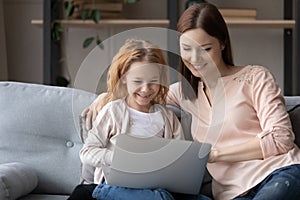 Smiling young mom and little daughter use laptop