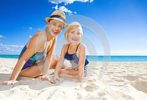 Smiling young mother and daughter in swimwear on seacoast