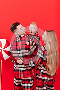smiling young mother and father are kissing and hugging their baby boy on red background. concept of love and