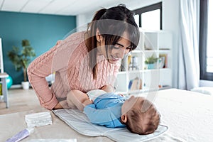 Smiling young mother has fun with little baby while changing his nappy at home