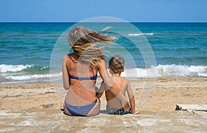 Smiling young mother kisses baby near the sea. Happy summer days.