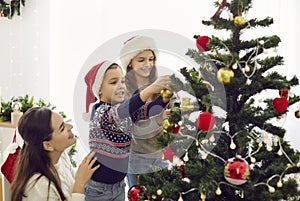 Happy mom and kids decorate Christmas tree at home