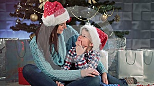 Smiling young mother and little cute child hugging sitting together and talking near Christmas tree