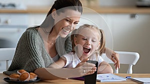 Smiling young mother showing funny cartoons to overjoyed daughter.