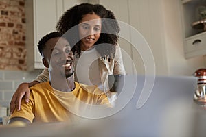 Smiling young multiethnic couple using a laptop together in their kitchen
