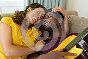 Smiling young multiracial couple romancing while lying with guitar at home