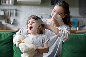 Smiling young mum making ponytail to little daughter