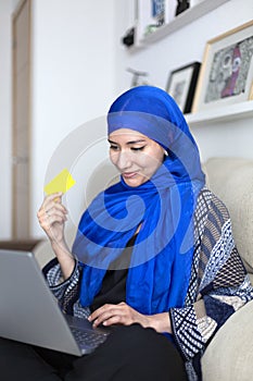 Smiling young muslim woman shopping online from home with credit card