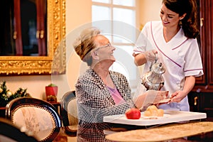 Smiling young nurse brings breakfast to senior woman at nursing