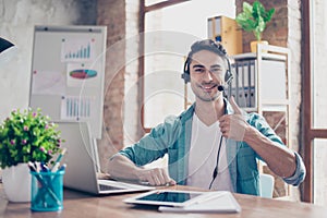 Smiling young operator of call center sitting at the table and s