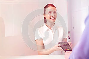 Smiling young patient paying fees through credit card at checkout counter in clinic