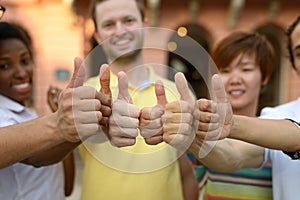 Smiling young people giving thumbs up sign